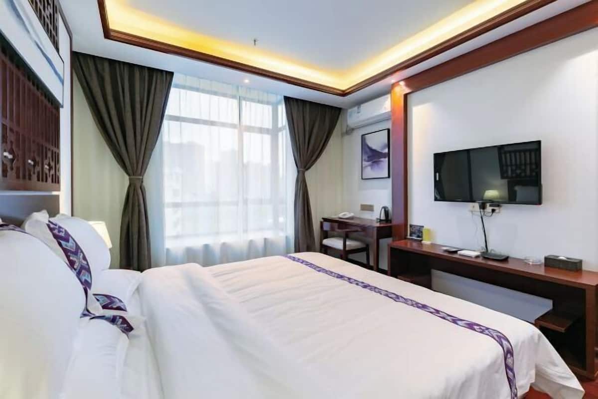 A hotel room with a bed, a desk, a chair, a television, and curtains.