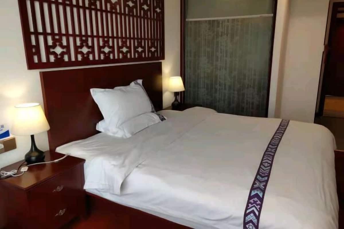 A neatly made bed with white linens and a decorative pillow, a wooden headboard, and a nightstand with a lamp.