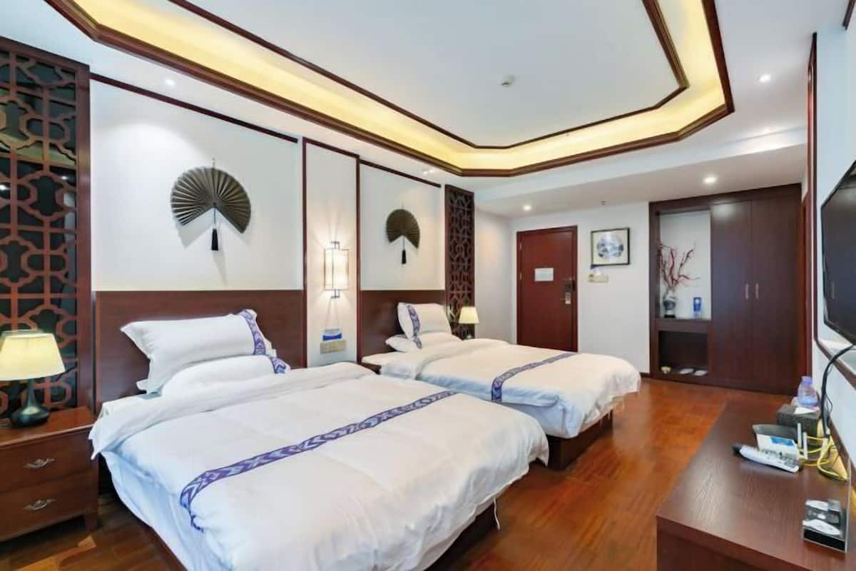 A hotel room with two beds, a wooden floor, a TV, and a bedside table with a lamp.