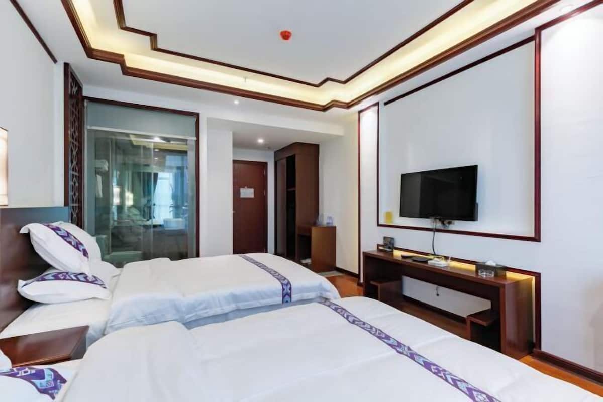 A hotel room with two beds, a TV, a desk, and a glass partition.