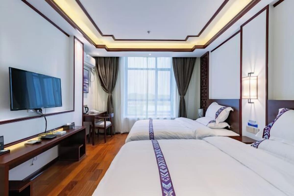 Habitación de hotel con dos camas, televisión, escritorio y ventana con cortinas.