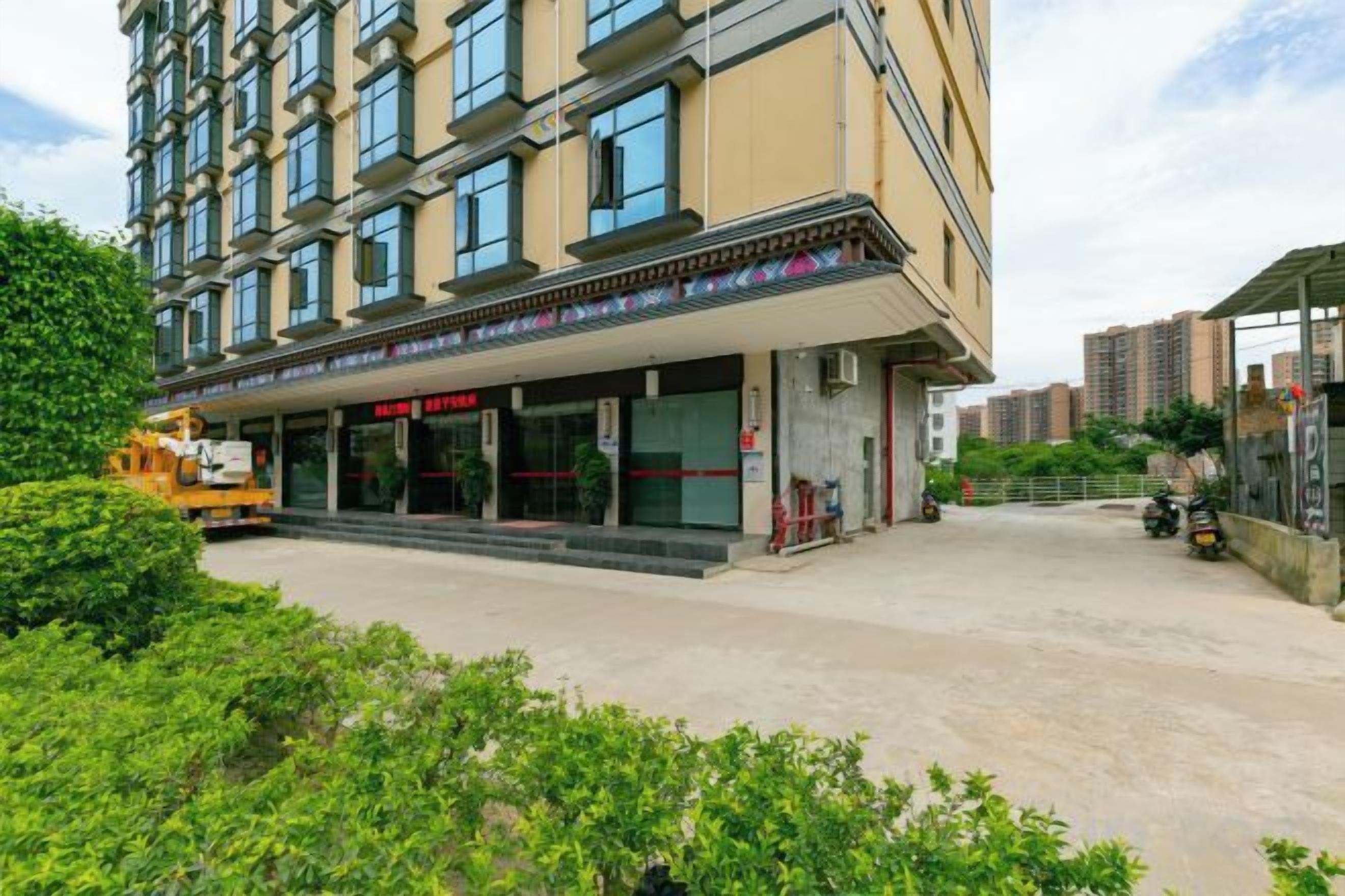 A multi-story hotel with a covered entrance, a parking area, and a construction vehicle nearby.