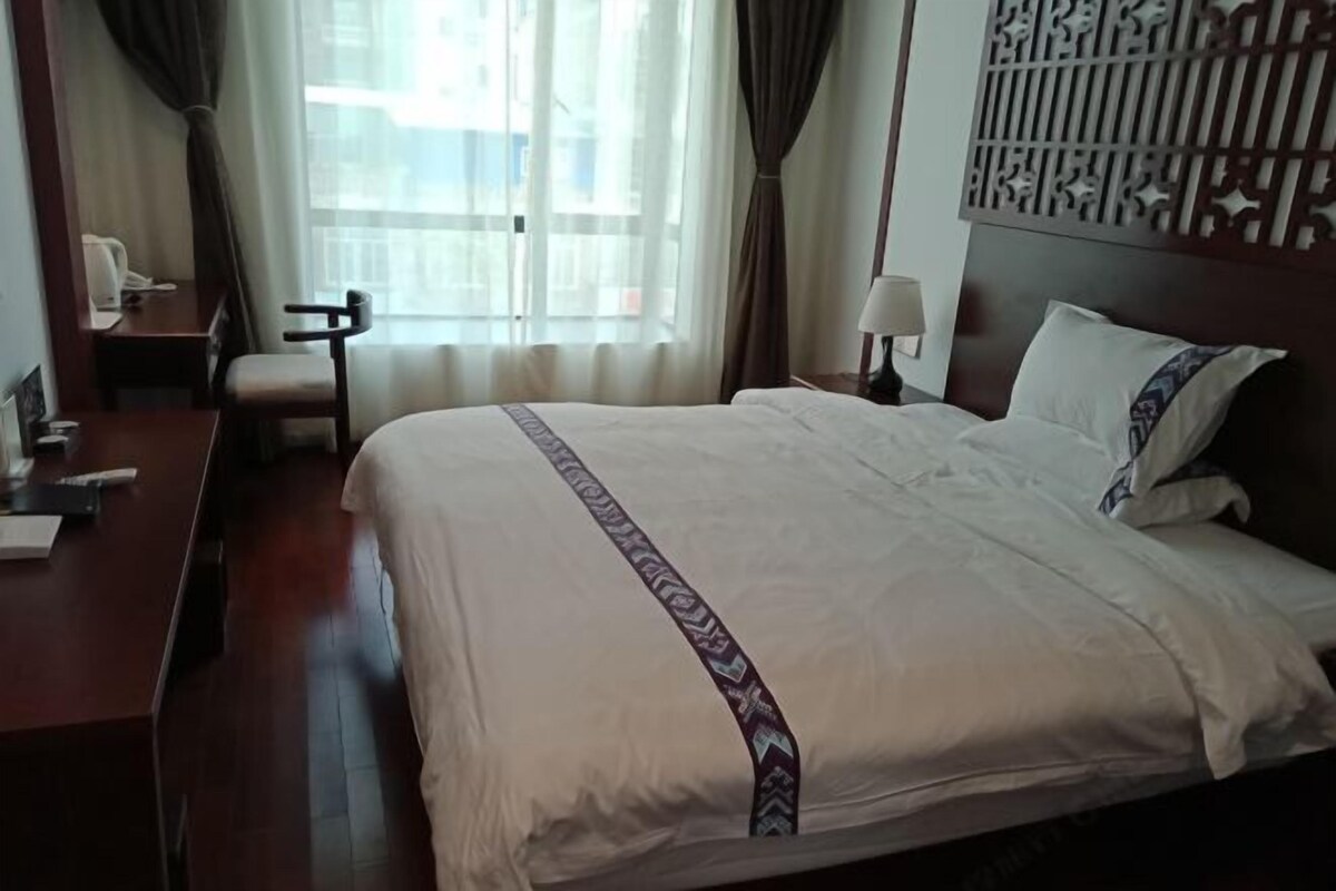 Habitación de hotel con una cama grande, un escritorio, una silla, una lámpara y vistas a la ciudad desde la ventana.