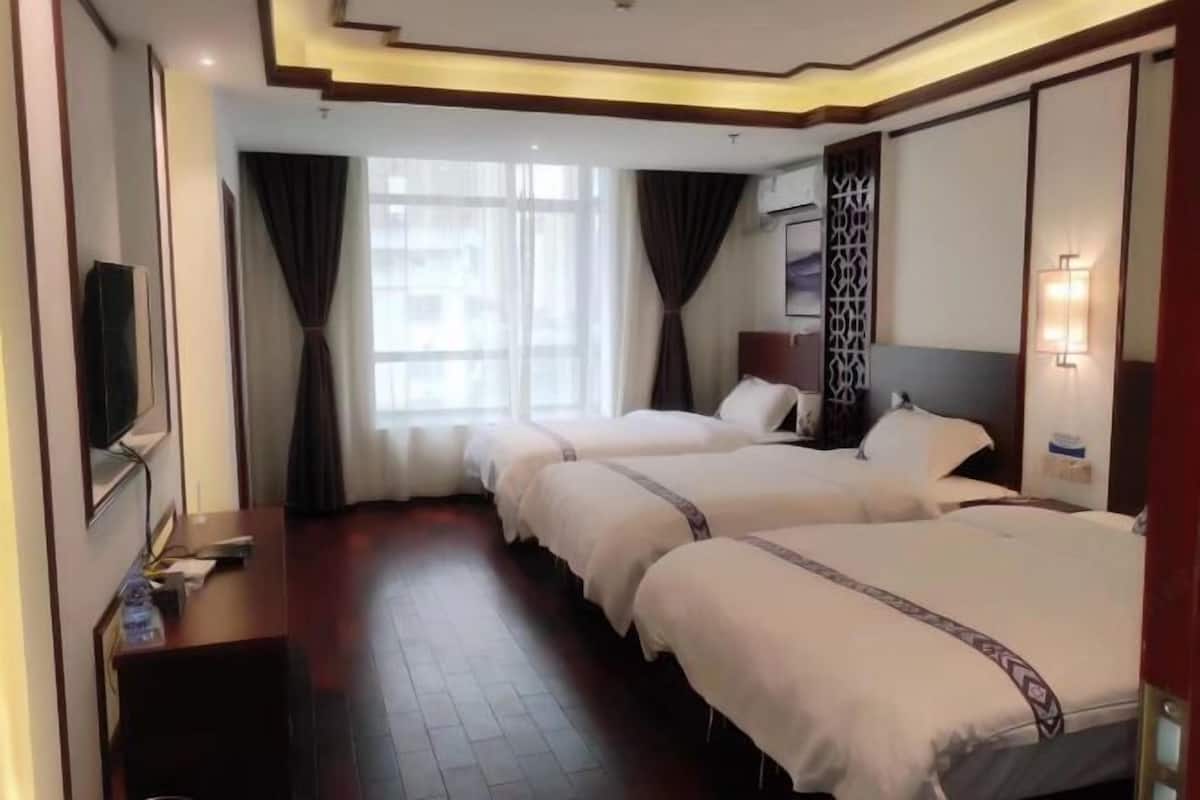 A hotel room with two beds, a TV, a desk, and a window with curtains.
