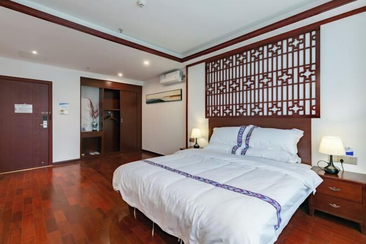 Habitación de hotel con una cama grande, suelo de madera, un separador decorativo y una mesita de noche con lámpara.