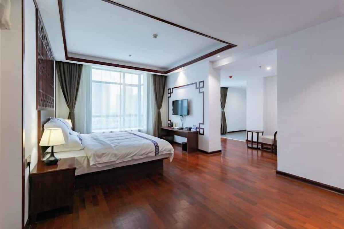 A modern hotel room with a large bed, a desk, a TV, and a chair.
