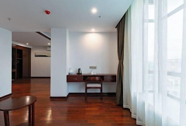 Una habitación de hotel moderna con piso de madera, un escritorio con silla, un ventanal con cortinas translúcidas y un equipo de aire acondicionado a la vista.