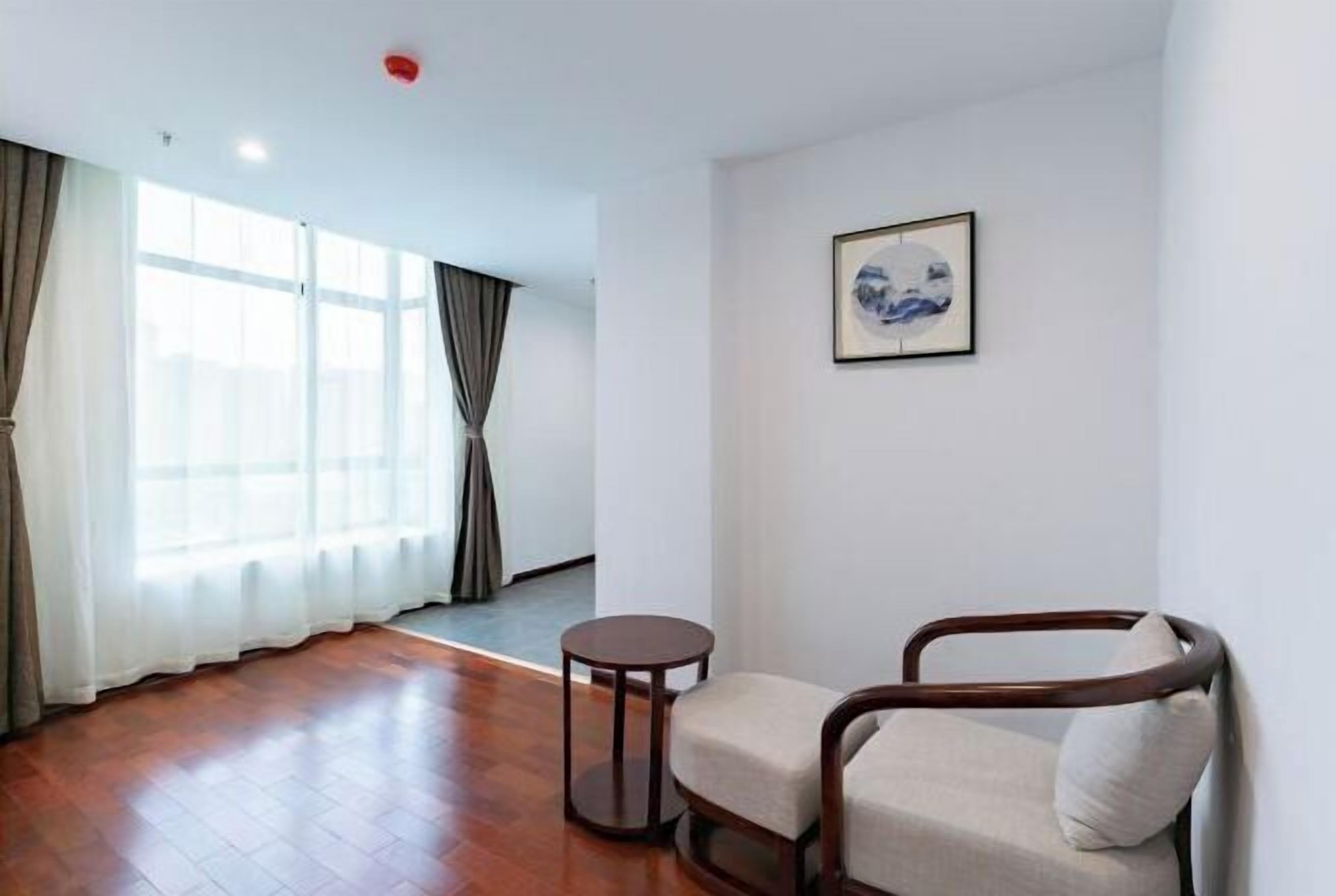 A room with a wooden floor, a round table, a cushioned chair, and a framed picture on the wall.