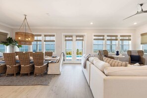 Un salon spacieux avec un grand canapé, un coin repas doté de chaises en osier et une vue sur la piscine, visible à travers des portes vitrées.