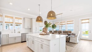 A spacious kitchen with white cabinetry, a large island, and hanging wicker pendant lights. - Monterey Oceanfront Beach House (Port St. Joe)