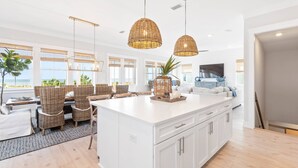 A spacious kitchen with a large island, wicker chairs, and pendant lighting. - Monterey Oceanfront Beach House (Port St. Joe)