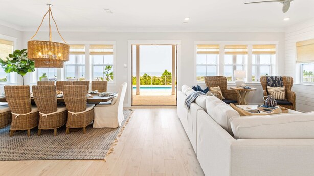 A spacious living room with a dining area, a large window with a view of a pool, and a ceiling fan. - Killarney Oceanfront Beach House Summer (Port St. Joe)