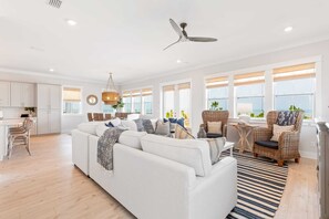 A spacious living room with a white sofa, wicker chairs, and a dining area with a table and chairs.