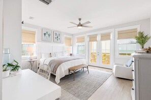 A spacious bedroom with a large bed, a ceiling fan, and a view of the outdoors through large windows.