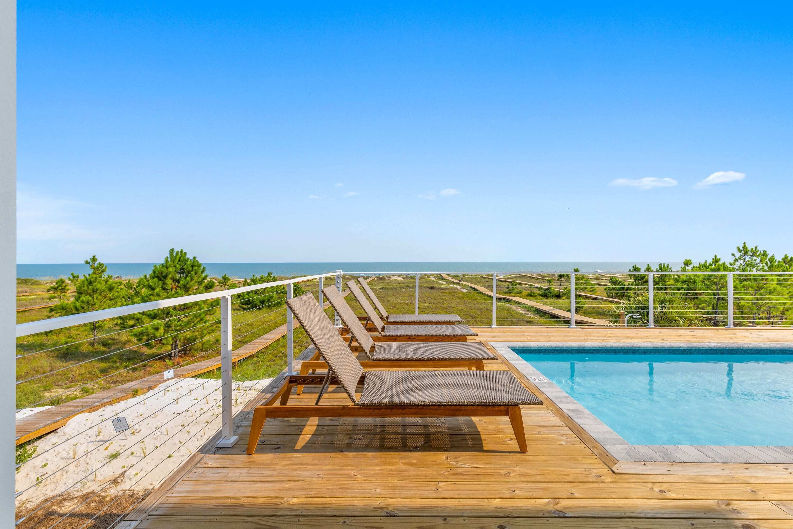 Terraza de madera con sillones de descanso con vistas a una piscina y al océano.