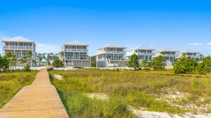 A wooden boardwalk leading to a row of beachfront houses with balconies. - Killarney Oceanfront Beach House Summer (Port St. Joe)