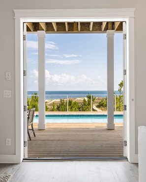 Vista desde una habitación con terraza de madera que da a una piscina, con vistas a una playa y al océano.