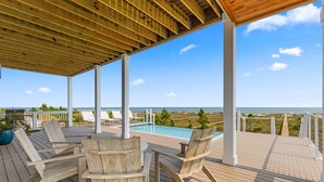 Um deck de madeira com área de estar externa, piscina e vista para o oceano.