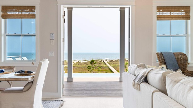 Uma sala de estar moderna com uma grande porta de vidro deslizante que dá para uma varanda com vista para o mar.