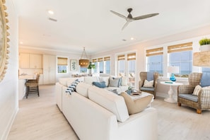 A spacious living area with a large sofa, wicker chairs, and a dining table. - Frazer Oceanfront Beach House with Elevated Infinity Pool! (Premier Bella Proper (Port St. Joe)