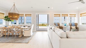 Uma sala de estar espaçosa com área de jantar, janelas amplas e vista para o oceano.
