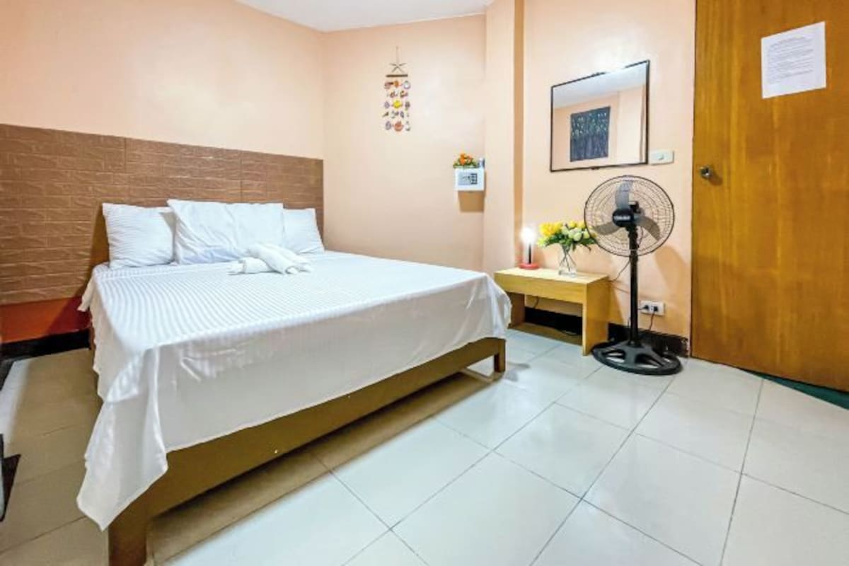 Une chambre d’hôtel avec un lit, une table de chevet avec une lampe, une horloge murale et une porte.