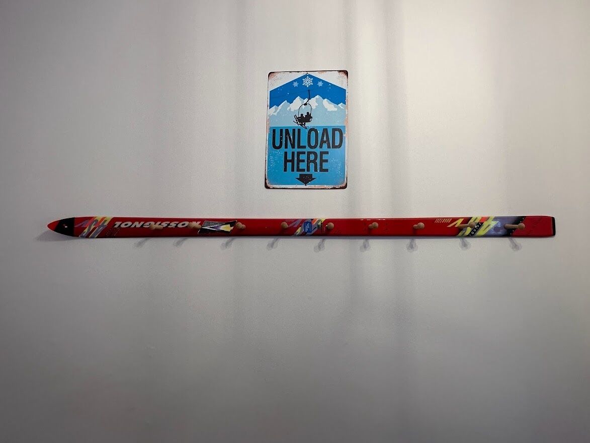 A red snowboard with a colorful design and the word "TONALSO" on it, placed on a white wall next to a sign that says "UNLOAD HERE".