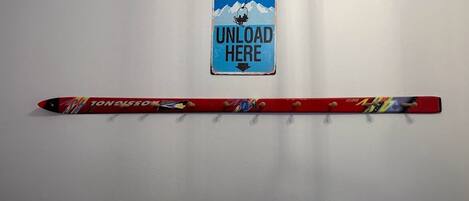 A red snowboard with a colorful design and the word "TONALSO" on it, placed on a white wall next to a sign that says "UNLOAD HERE".