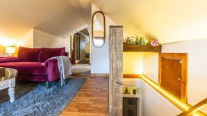 Ein Schlafzimmer im Dachgeschoss mit einem roten Sofa, einem Spiegel, Holzboden und einer Treppe mit einer Leuchte.