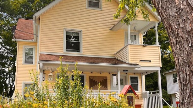 Ein zweistöckiges Haus mit Veranda, kleinem Balkon und weißem Zaun.