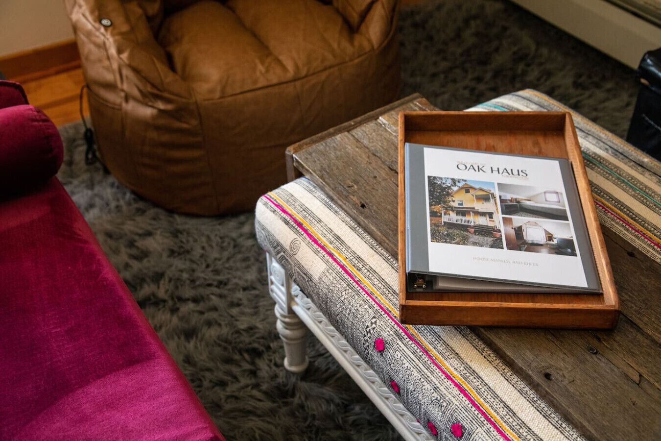 A framed book titled 'Oak Haus' on a wooden table with a patterned cushion and a brown leather chair in the background.
