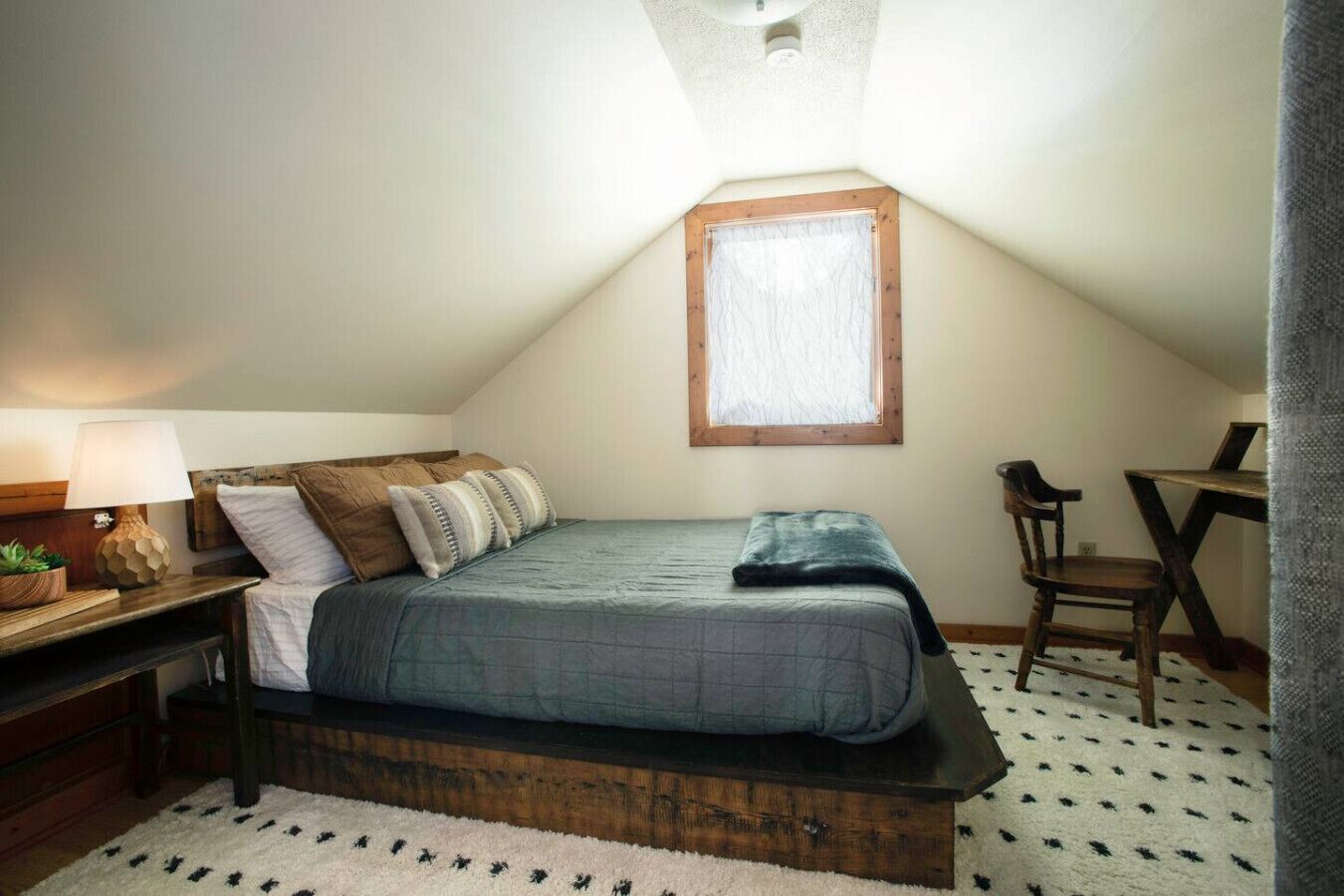 A bedroom with a bed, a desk, a chair, a lamp, and a window.