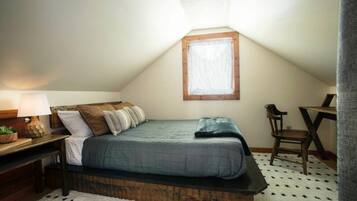 A bedroom with a bed, a desk, a chair, a lamp, and a window.