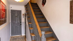 Eine Treppe mit Holzboden und einem grauen Geländer, eine graue Tür mit einem kleinen Schild und ein an der Wand befestigter Kranz.
