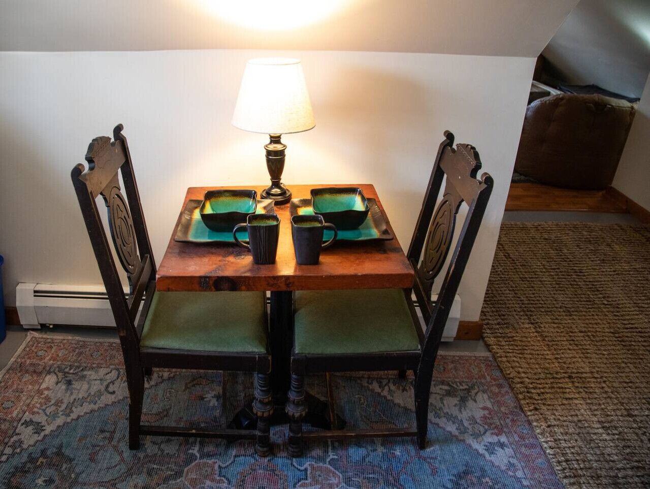 A dining table with chairs, a lamp, and two green mugs on a wooden table.