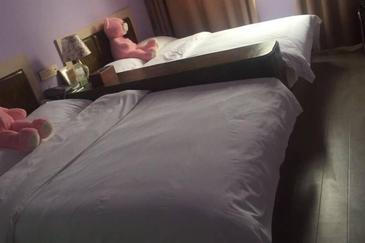 A hotel room with a bed, a nightstand, a lamp, and a pink stuffed toy.