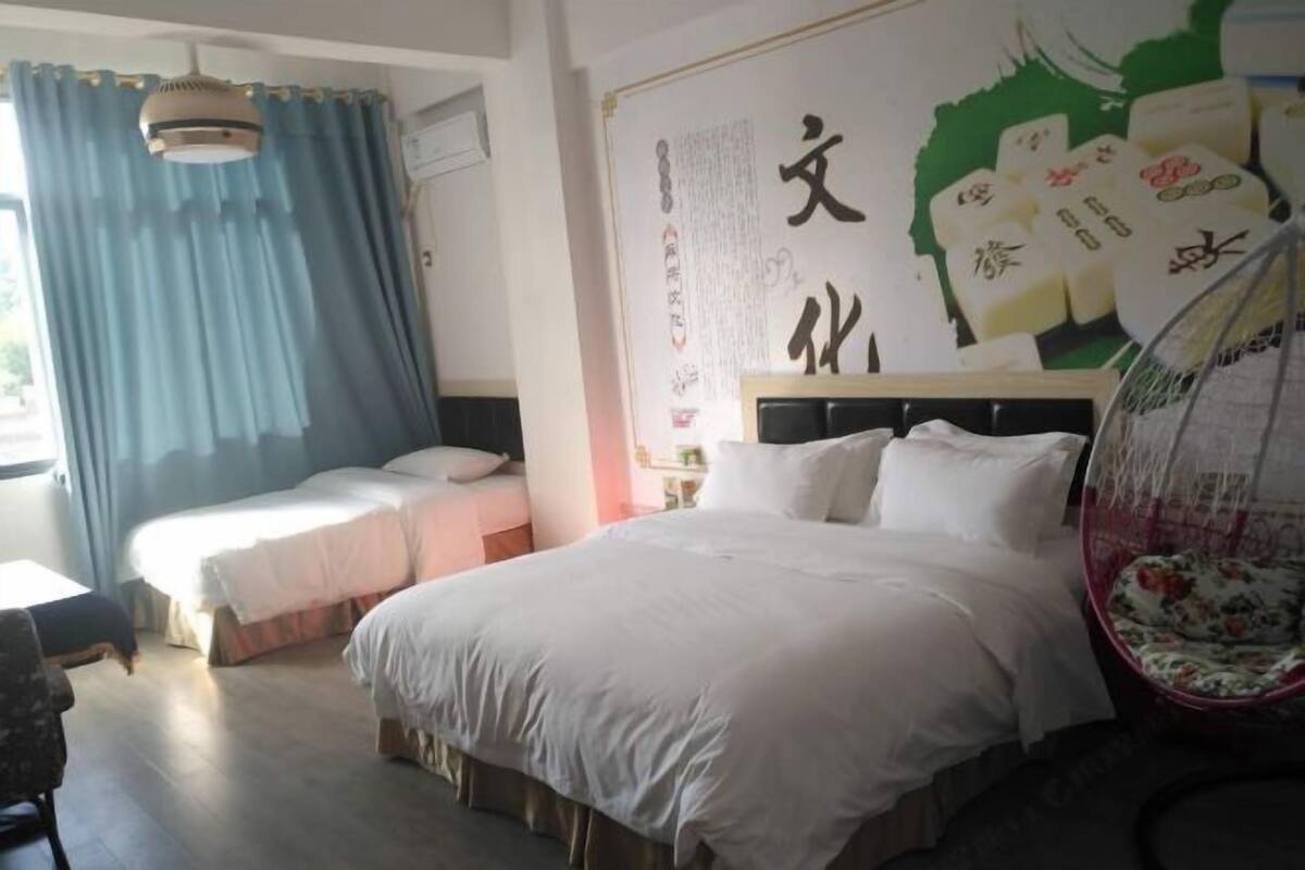 A hotel room with a large bed, a smaller bed, a desk, and a chair. There is a large poster on the wall and a window with curtains.