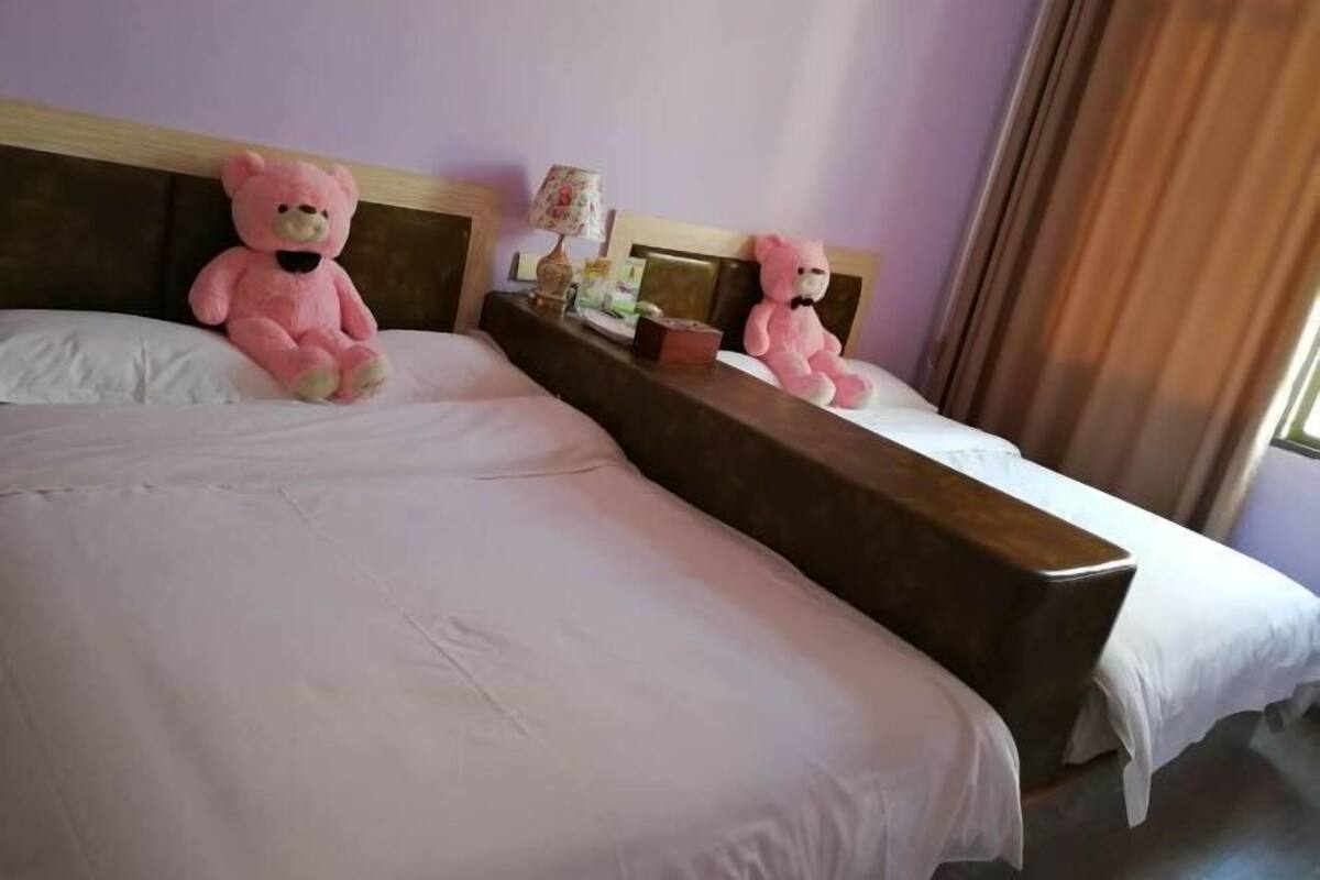 A hotel room with two beds, each with a headboard, a nightstand with a lamp, and a teddy bear on one of the beds.