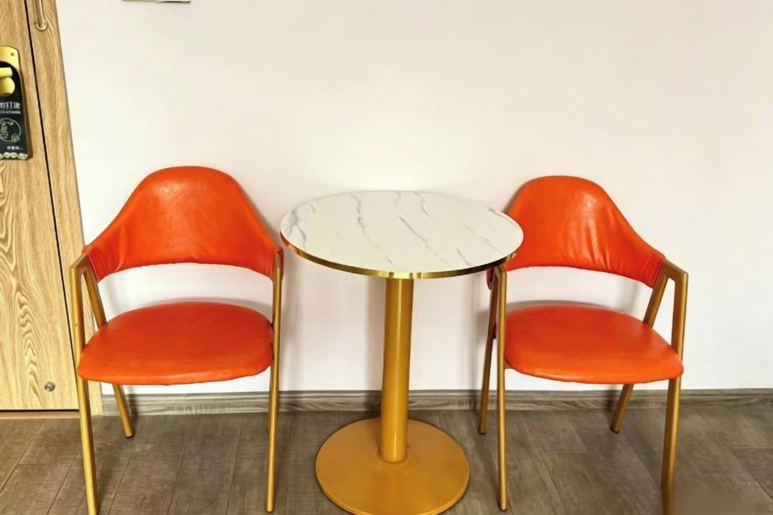 Ein Zimmer mit zwei orangefarbenen Sesseln und einem runden Tisch mit goldener Basis.