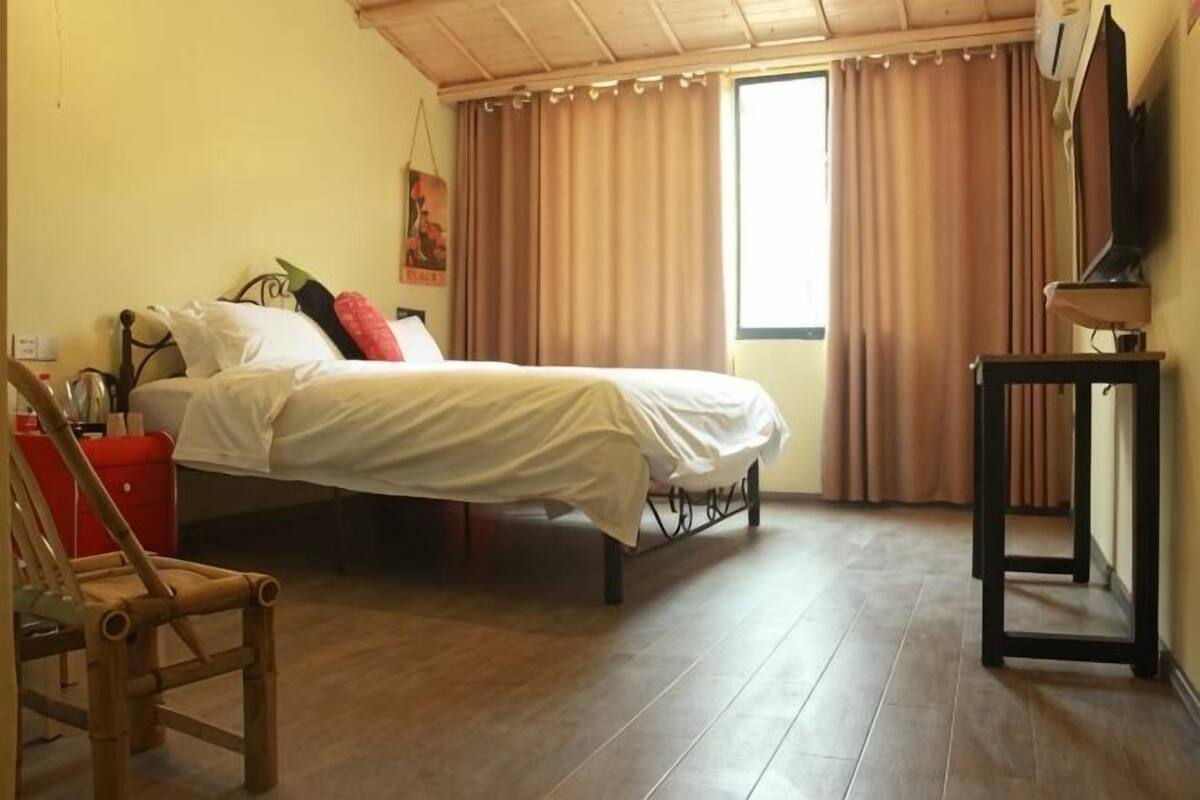 A bedroom with a bed, a chair, a TV, and a window with curtains.