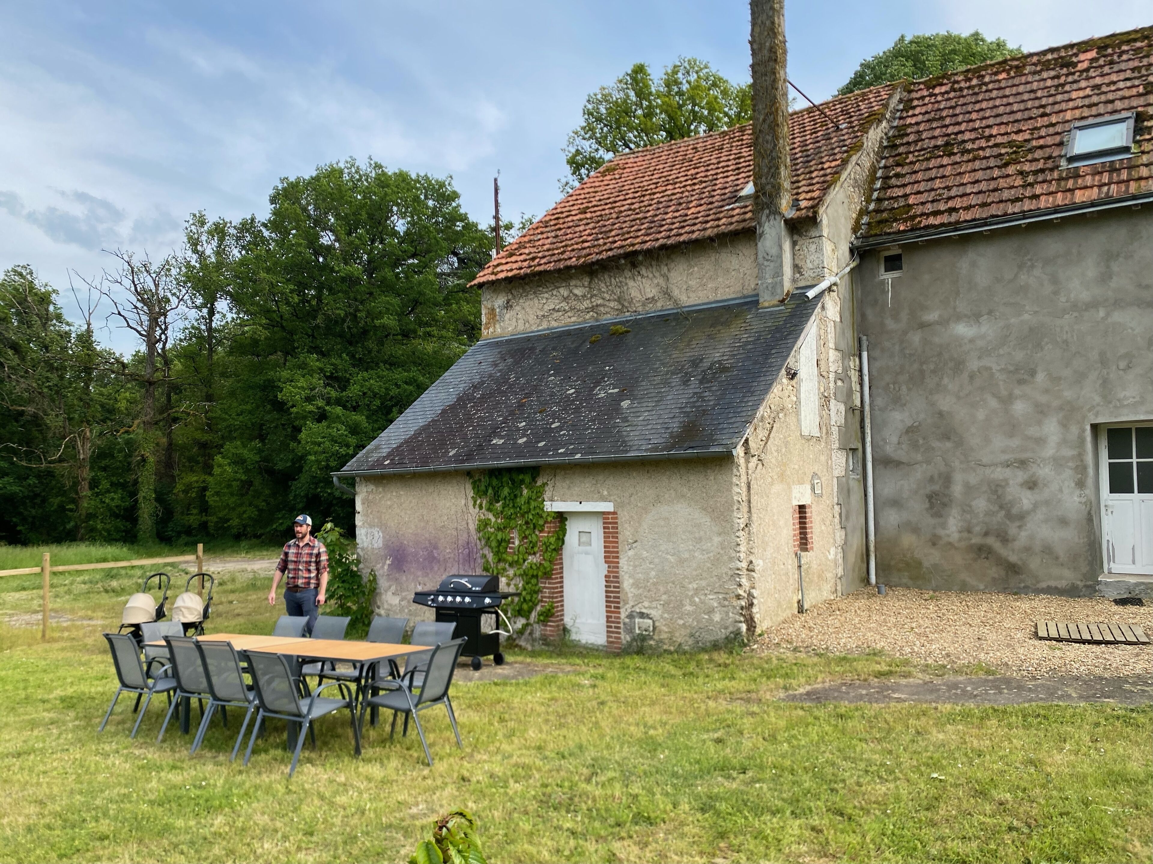 A rustic house with a tiled roof, a small porch, and a dining area with a table and chairs.
