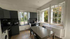 A modern kitchen with dark cabinets, a central island, and large windows offering a view of greenery.