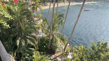 A balcony with lush greenery and a view of a beach with boats.