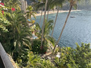 A balcony with lush greenery and a view of a beach with boats. - CASA SOL Premium Ocean View Oasis at La Jolla (Mismaloya)