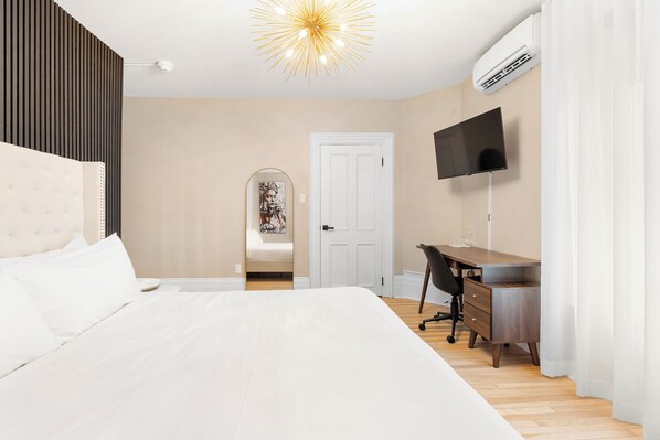 Un dormitorio con cama, escritorio, silla, televisor y unidad de aire acondicionado.