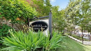 Letrero de hotel con un emblema circular y el nombre 'Hôtel Manoir de la Tour' rodeado de follaje.