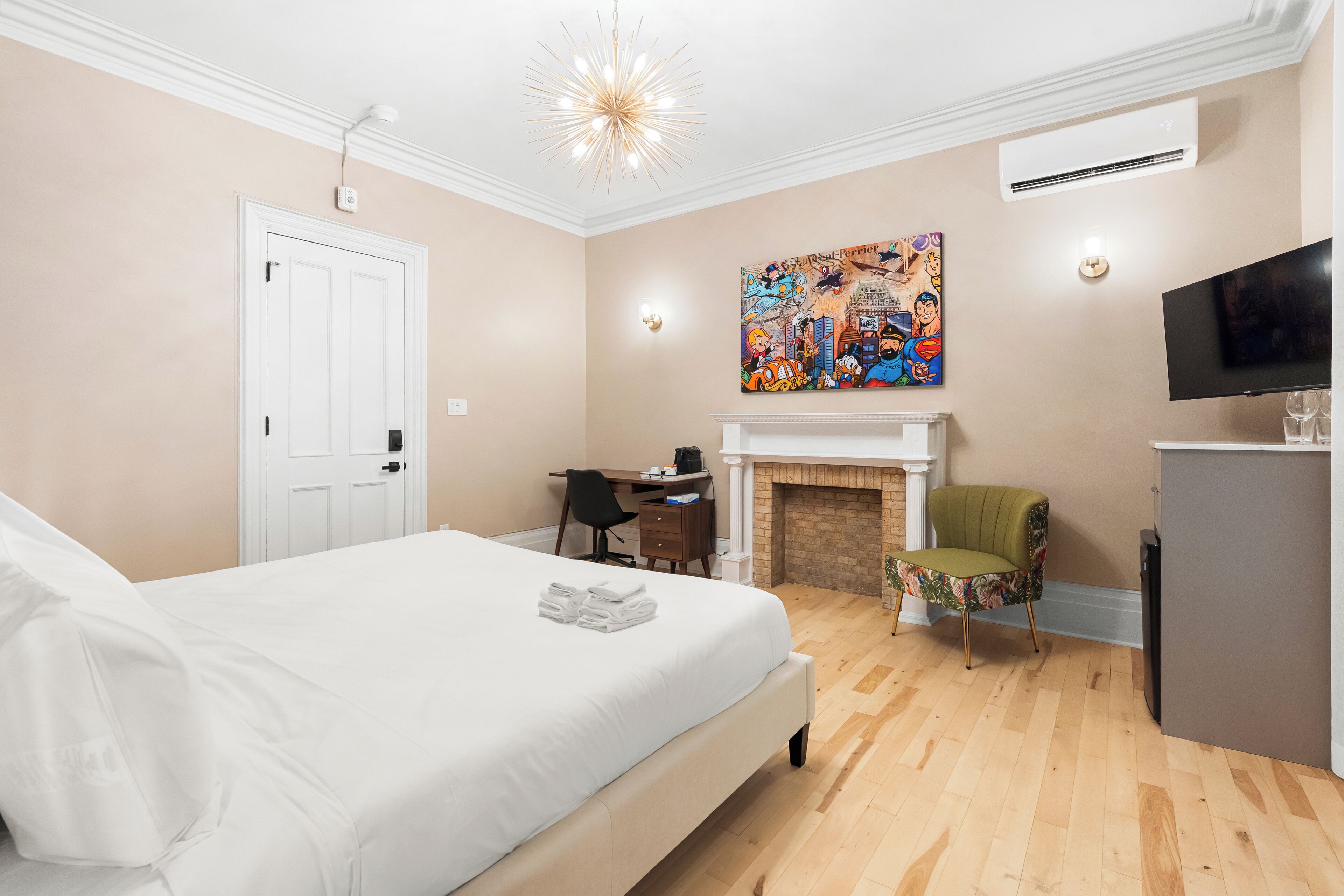 Habitación de hotel con cama, escritorio, silla, chimenea, televisor y obras de arte en la pared.
