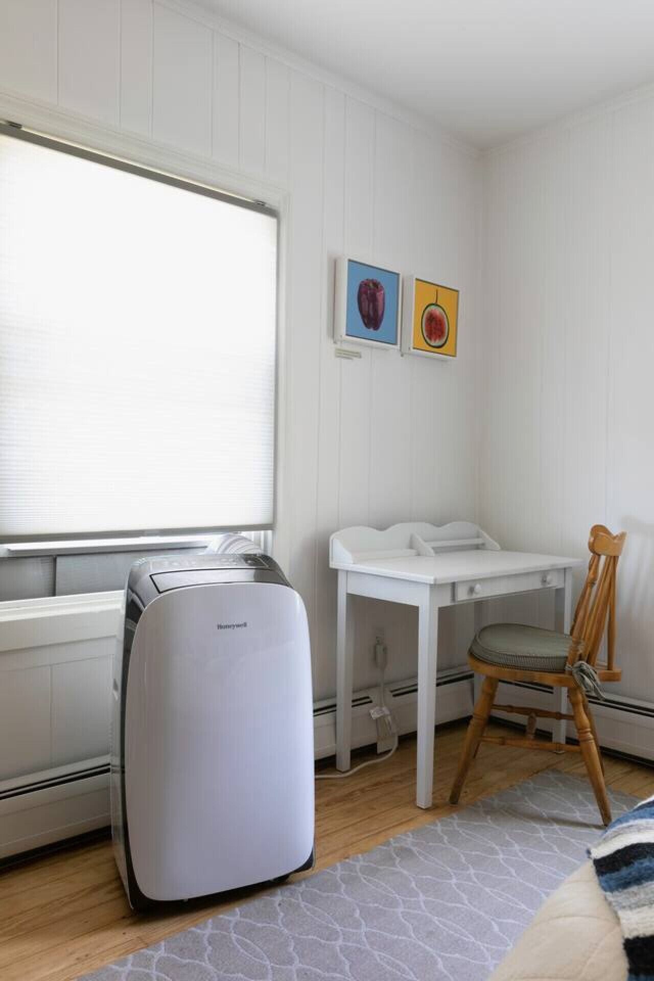 Ein kleiner, sauberer Raum mit einem weißen Heizkörper, einem Heizgerät, einem Tisch mit Stuhl und zwei gerahmten Bildern an der Wand.
