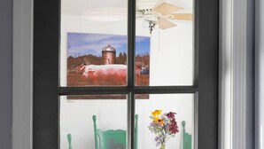 A door with a frosted glass panel featuring a landscape painting, a ceiling fan, and a table with a vase of flowers. - Cozy Modern Farmhouse Private Apt - 3 Beds (Torrington)