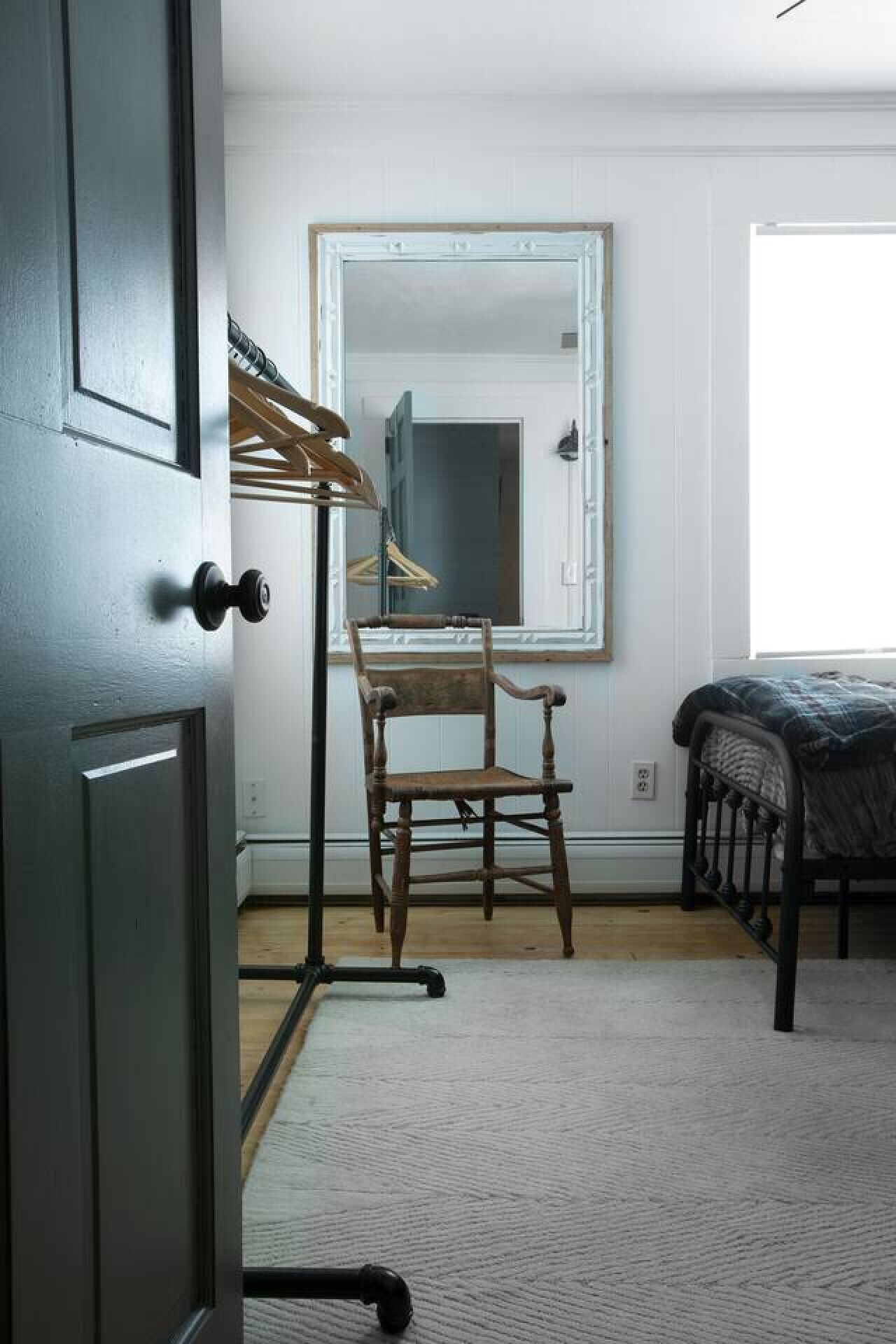 A bedroom with a wooden chair, a bed, a mirror, and a door.